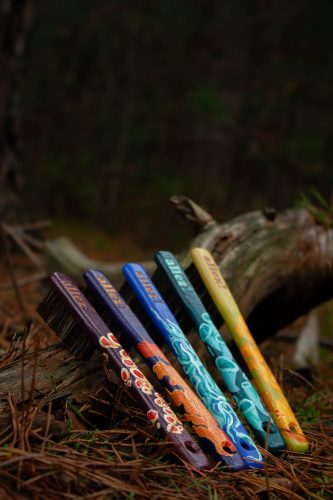 vijf beschilderde borstels op een bosgrond met dennennaalden en boomtakken